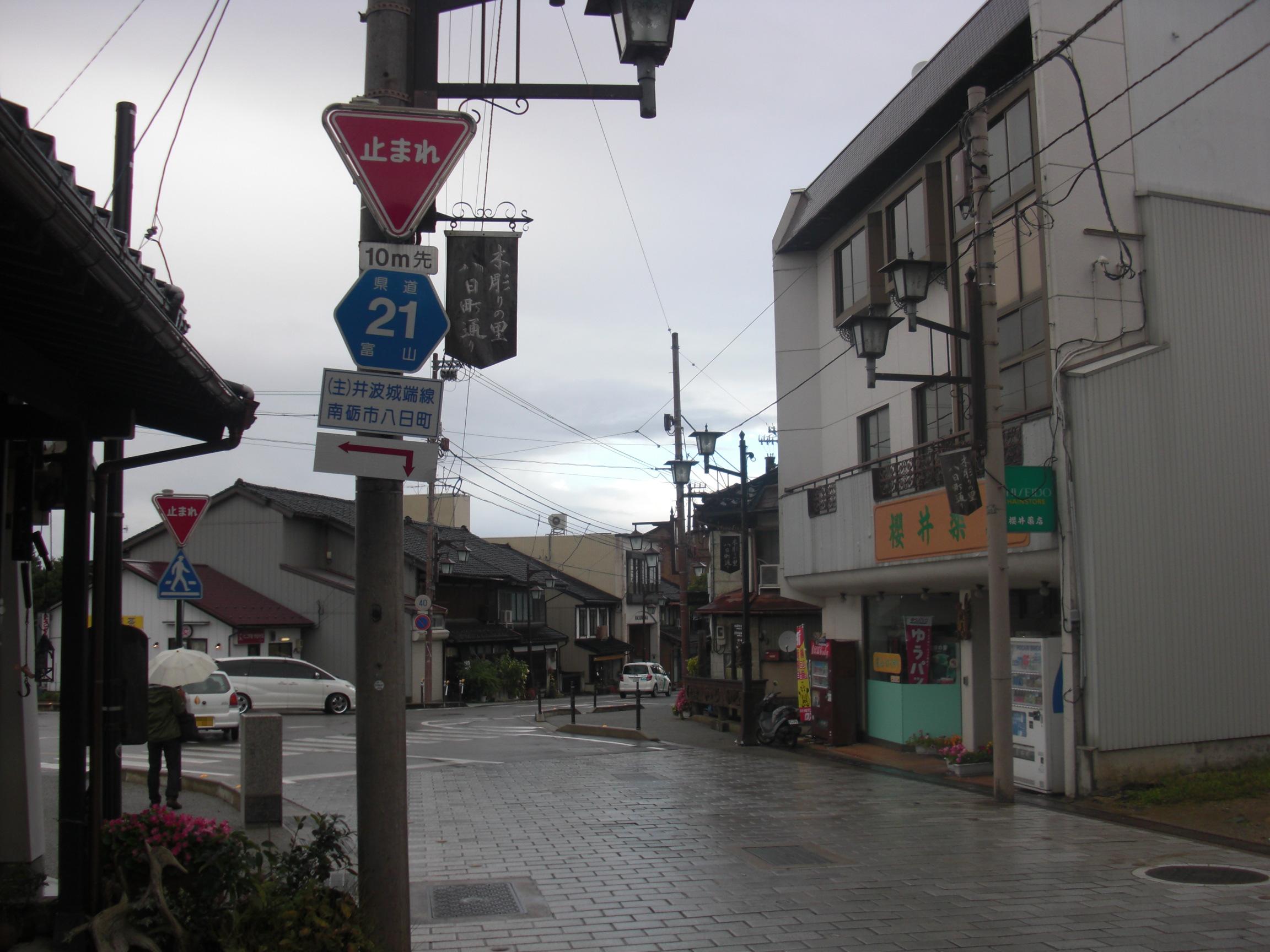 八日町通りの石畳と、県道21号の標識、道沿いに続く店
